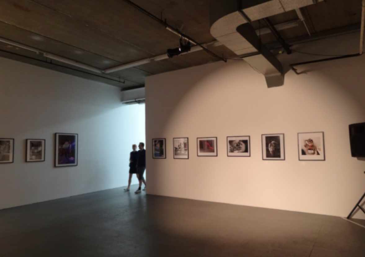 Pictured is a wall of framed graphic designs and photos of the band on a white wall, with two people approaching.