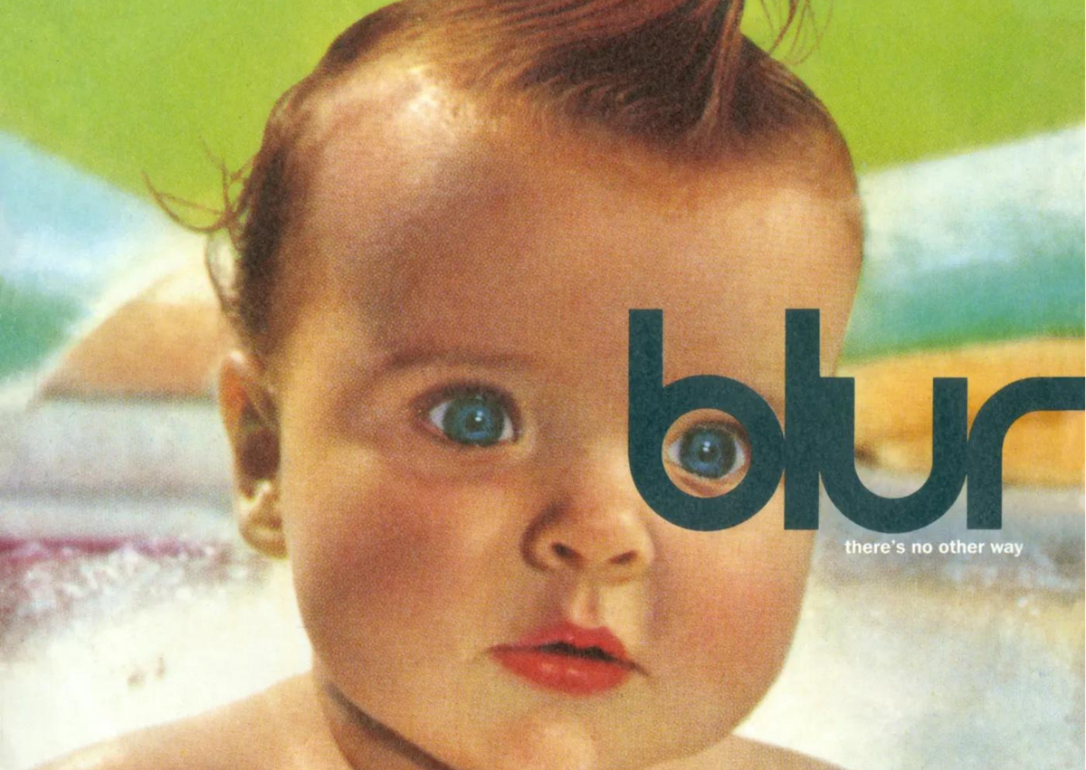 Pictured is a baby in front of a green, blue, yellow and pink background, with the word "Blur" covering the left side of its face.
