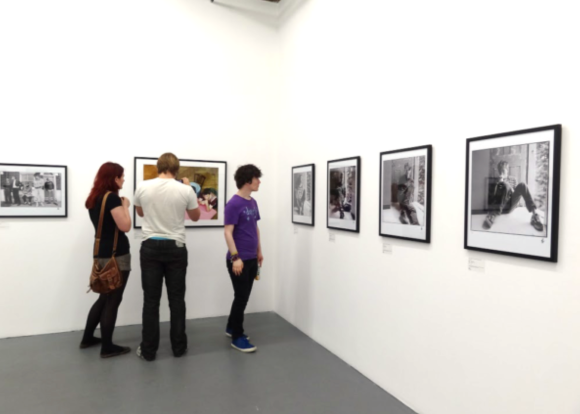 Pictured is a wall of framed black and white photos and graphic designs of the band, with 3 people observing them.