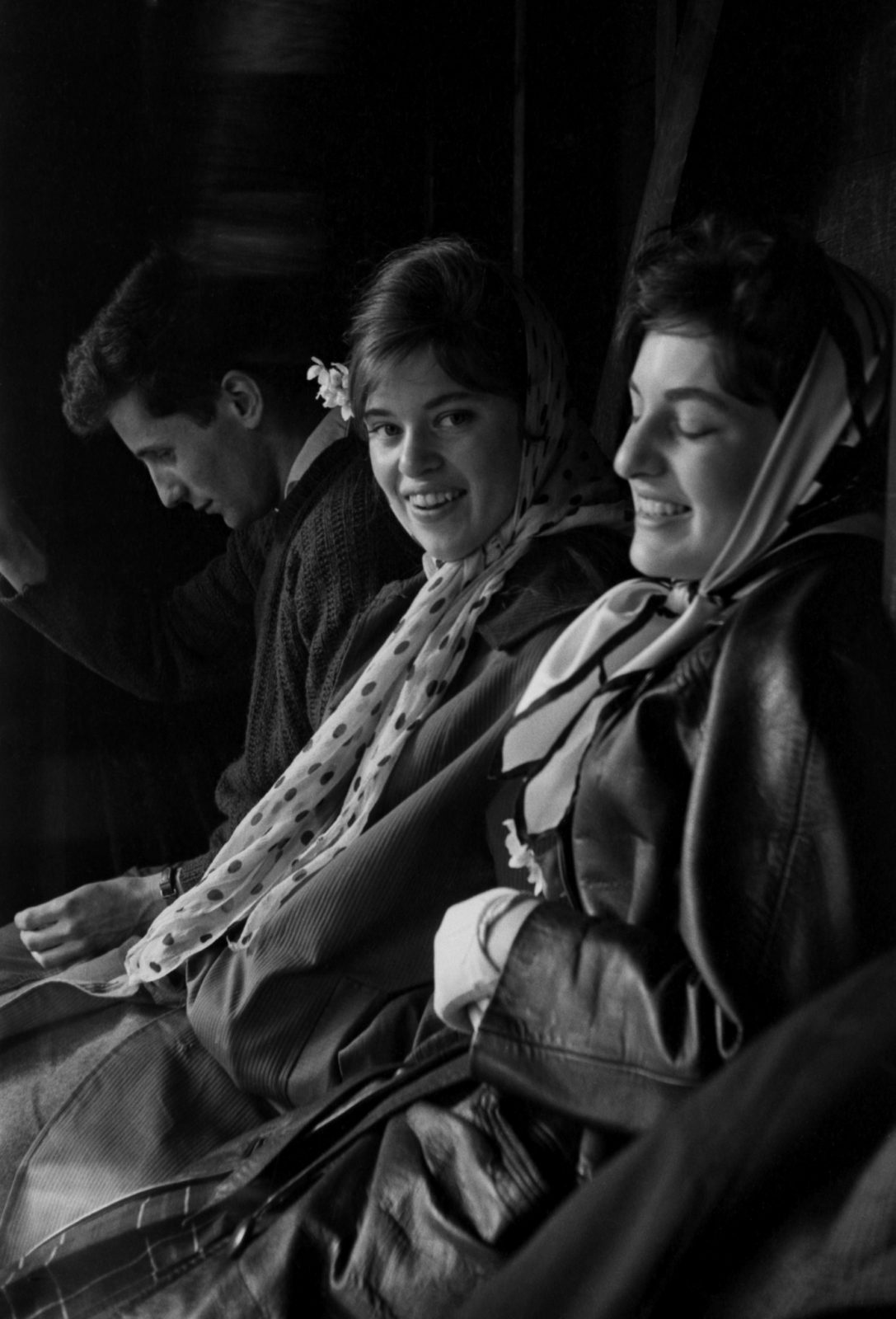 One man in shadows with his head down with two women next to him grinning and seemingly laughing coming into the light with more of their self on display in the light