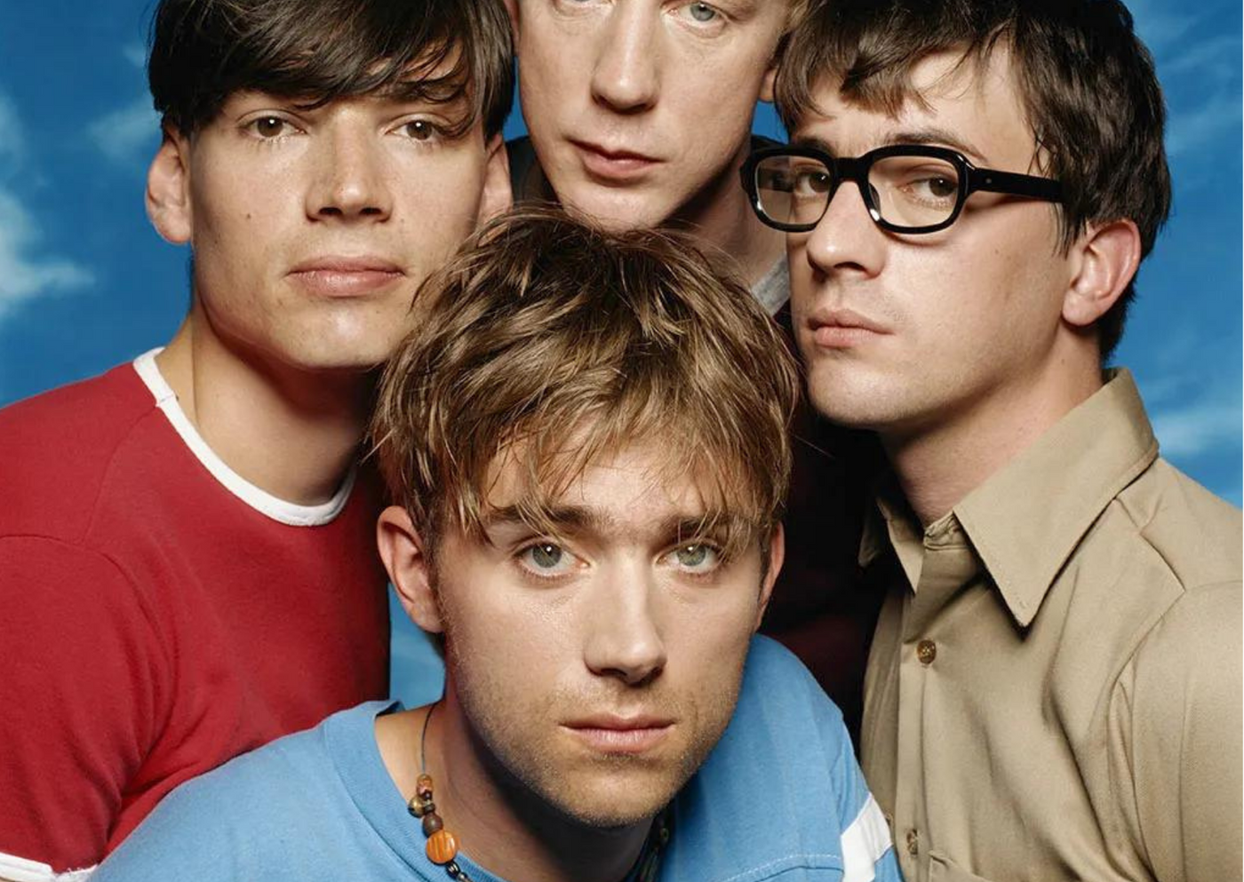 Pictured are the four members of Blur, Alex James, David Rowntree, Graham Coxon and Damon Albarn (clockwise beginning from far left) looking into the camera in front of a blue background.