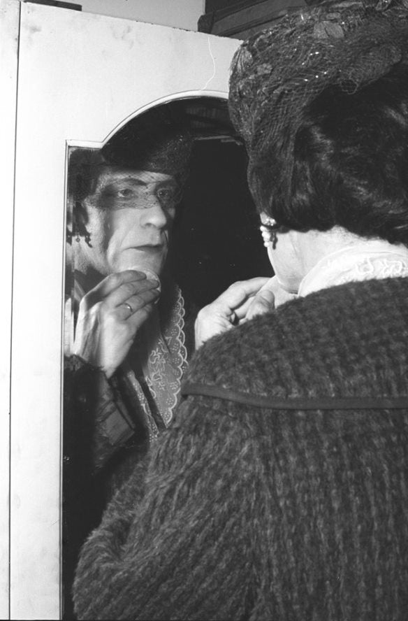 A newly found woman embracing her face in the mirror seeming to have arranged her hat and makeup