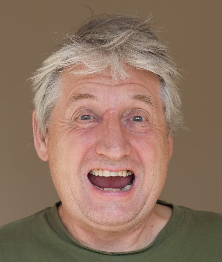 A profile of a teethy grinning Storm Thorgerson with a coffee coloured background
