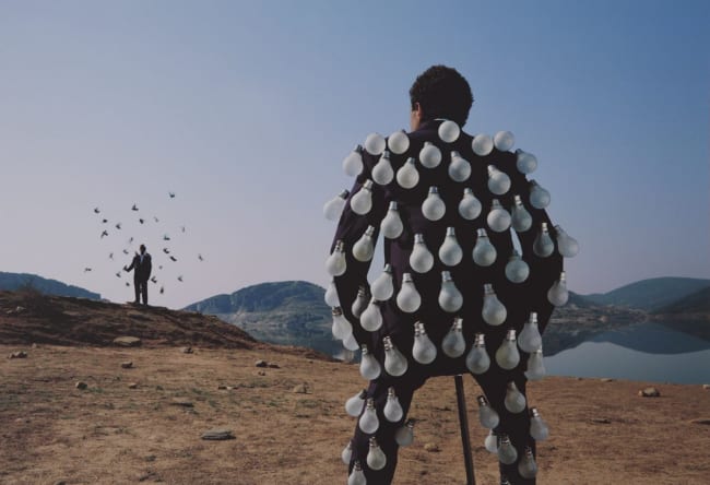 a man covered in light bulbs closest to the perspective and a man on a hill in the distance surrounded by birds